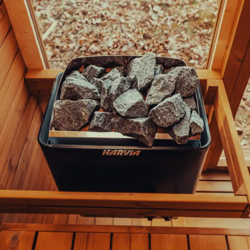 Black container with sauna stones on a wooden surface, featuring the Harvia brand.